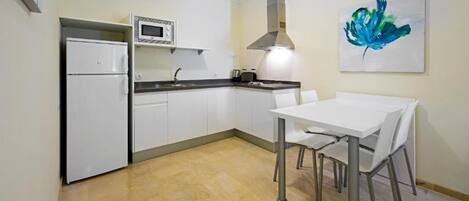 Una cocina compacta con armarios blancos, un microondas, una estufa y un comedor con mesa y sillas.