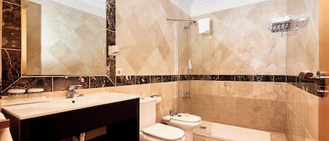 A bathroom with a large mirror, two toilets, a sink, and a shower area.
