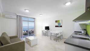 A modern living room with a sofa, a dining area with chairs, a TV, and a kitchen with a sink and stove. - Kn Aparthotel Panoramica Heights (Adeje)
