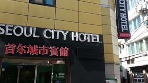 Das äußere Erscheinungsbild des Seoul City Hotels mit moderner Fassade, großen Fenstern und einem Verkaufsautomaten am Gehweg.