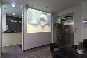 A hotel reception area with a digital screen displaying a cityscape, an elevator, and a reception desk.