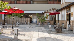 A courtyard with stone pathways, red umbrellas, and traditional Japanese elements like a large pot and wooden fences.