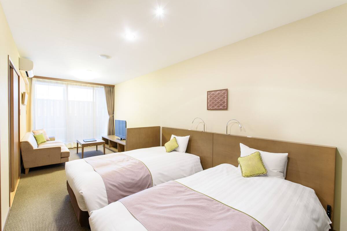 Habitación de hotel con dos camas, un sofá, un escritorio y un televisor.