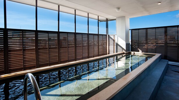 A modern indoor swimming pool with a glass barrier and metal railings, large windows, and a view of the sky.