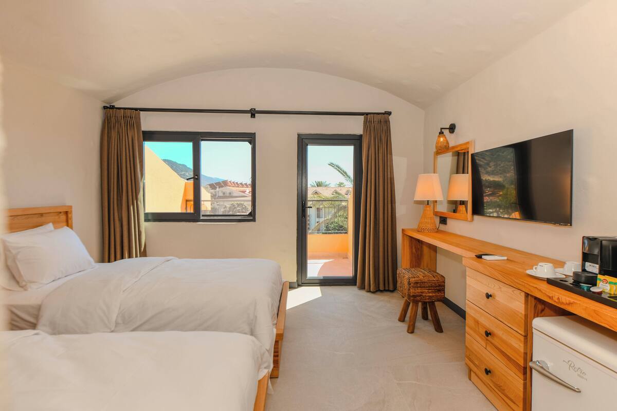 Una habitación de hotel con dos camas, un escritorio con lámpara, cafetera y televisión.