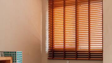 A bathroom with a bathtub, a window with blinds, and a tiled wall.