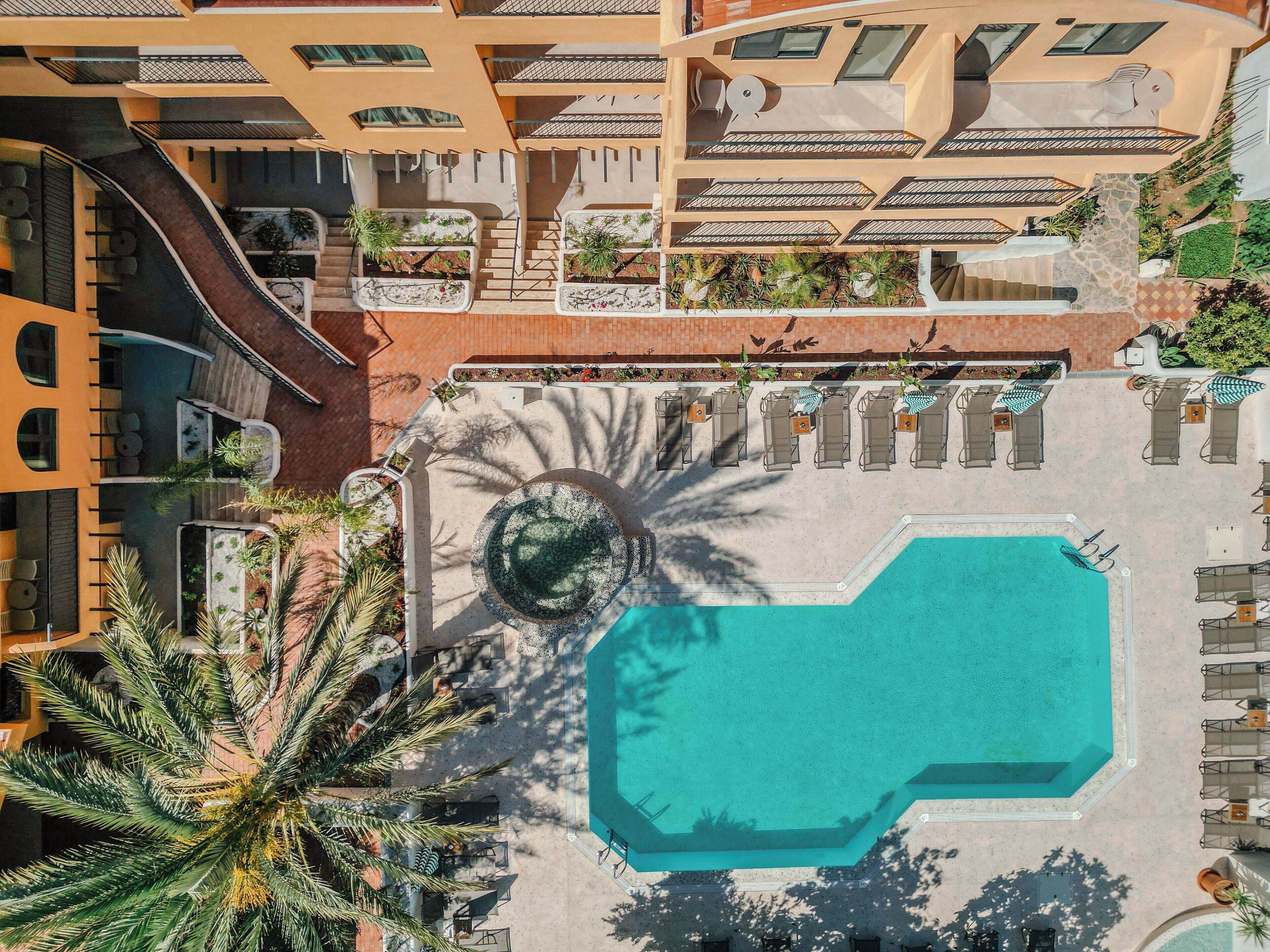 An aerial view of a resort with a central pool, multiple balconies, and outdoor seating areas.