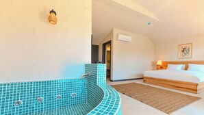 A bedroom with a large bed, a bathroom with a blue-tiled bathtub, and a wooden headboard. - Ünsal Hotel (Fethiye)