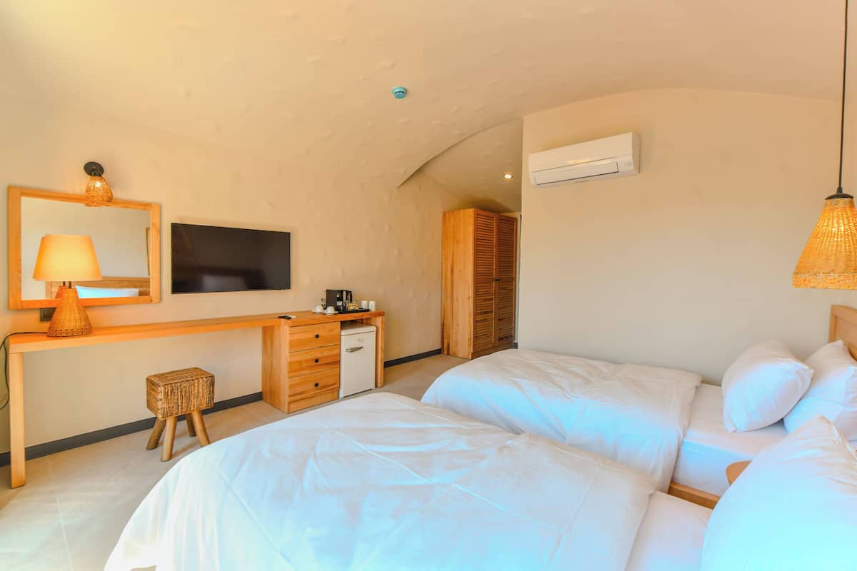 Un dormitorio con dos camas, un escritorio con lámpara, televisión y aire acondicionado.
