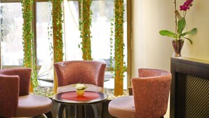 A room with three pink chairs, a small table with a vase of flowers, and a window with green vines. - Hotel Vozarev (Belgrade)