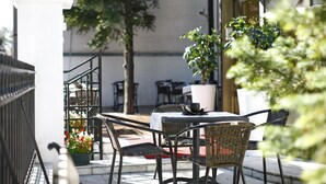 An outdoor patio with a table and chairs, surrounded by potted plants and a railing. - Hotel Vozarev (Belgrade)
