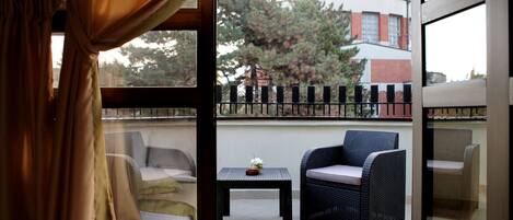 A balcony with wicker furniture, a small table with a flower, and a view of a building and trees.