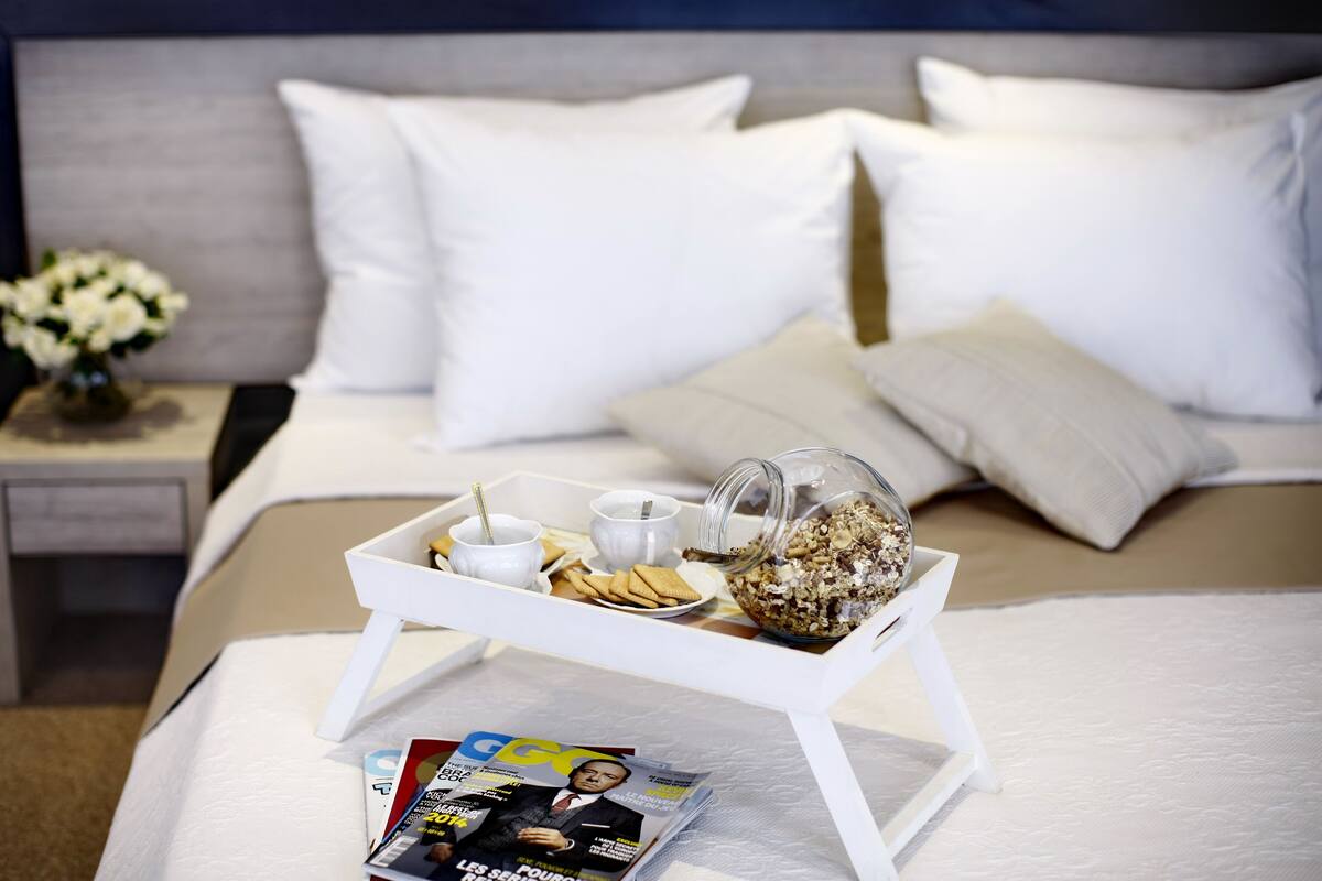 A neatly made bed with white linens, a tray with breakfast items, and a magazine on the bed.