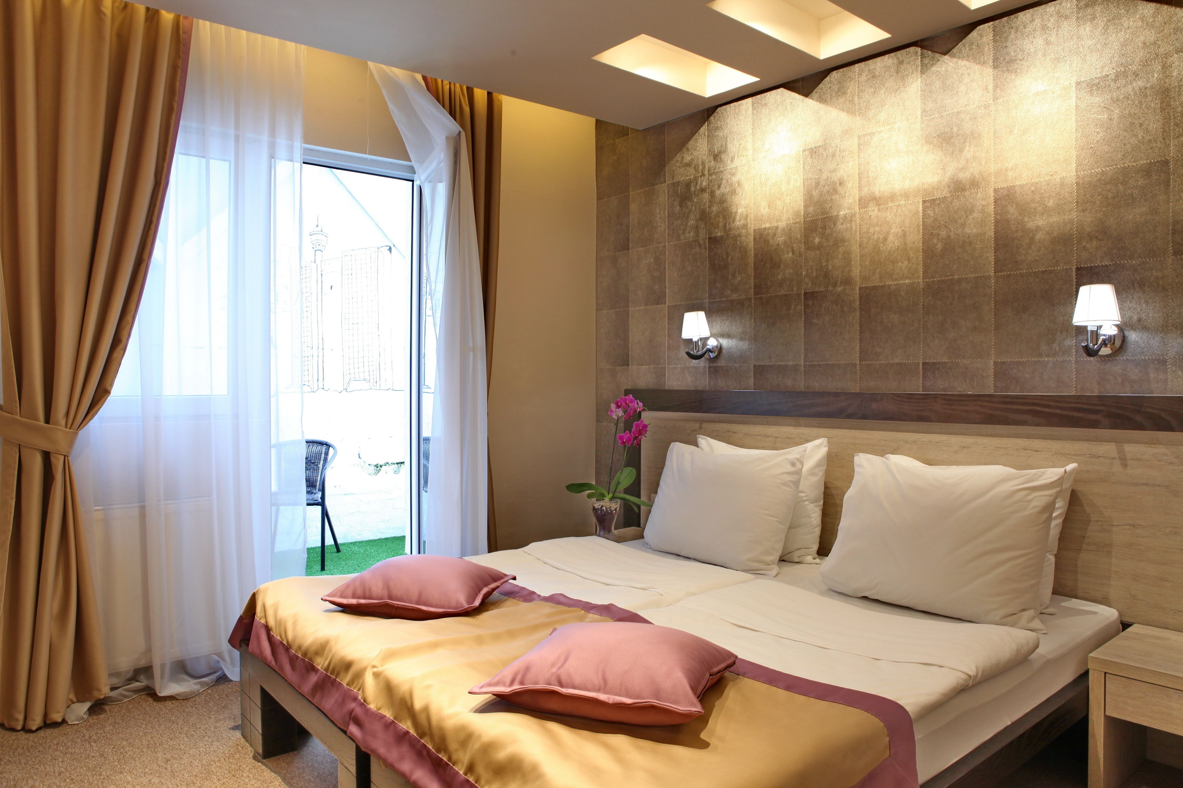 Habitación de hotel con cama, cortinas, mesita de noche, lámpara y vista a un edificio.