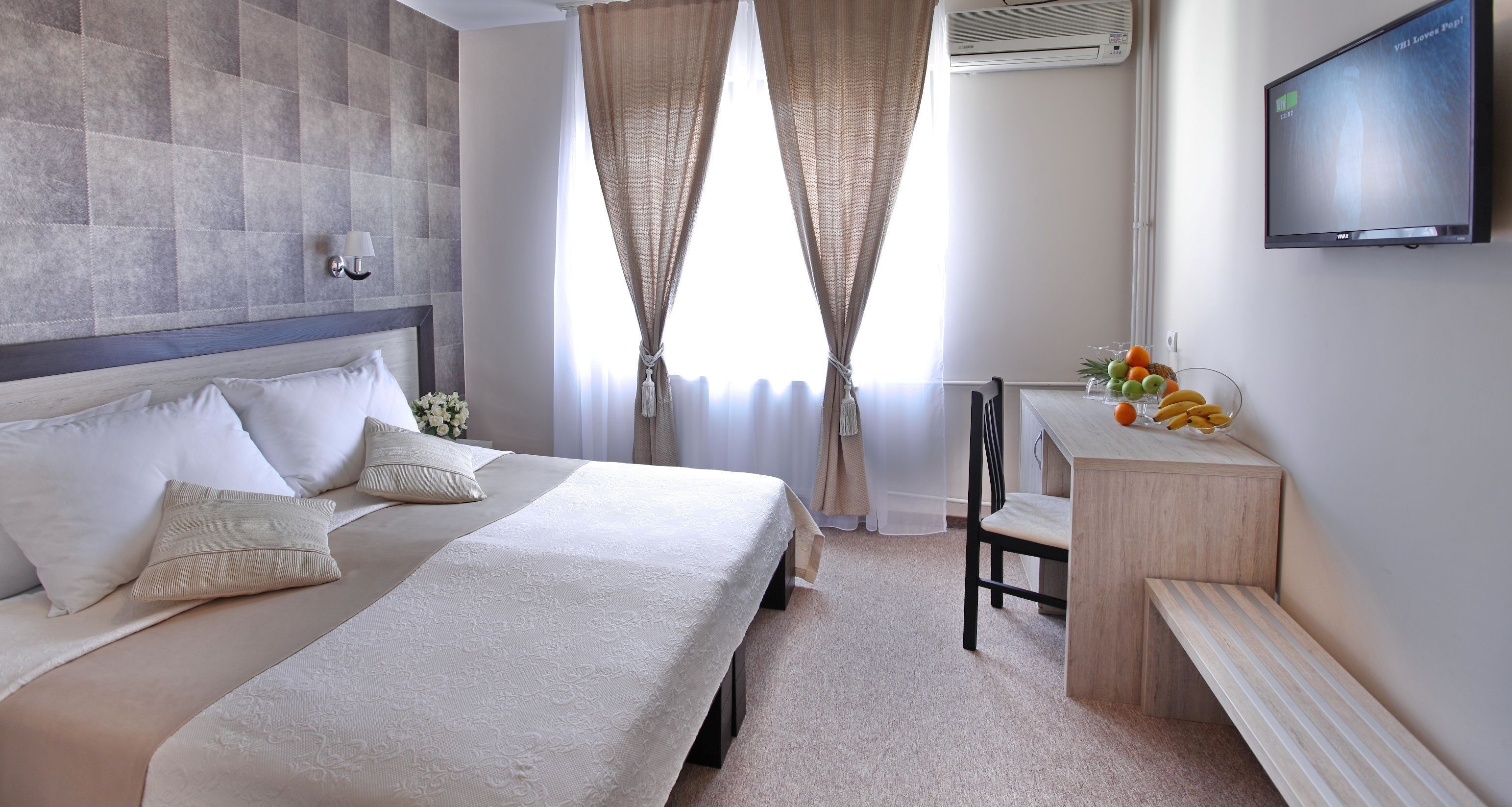 Une chambre d’hôtel avec un grand lit, un bureau avec une chaise et un téléviseur fixé au mur.