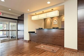 A reception area with a wooden reception desk, a glass door entrance, and a welcome mat. - Sleep Inn & Suites Fort Scott (Fort Scott)