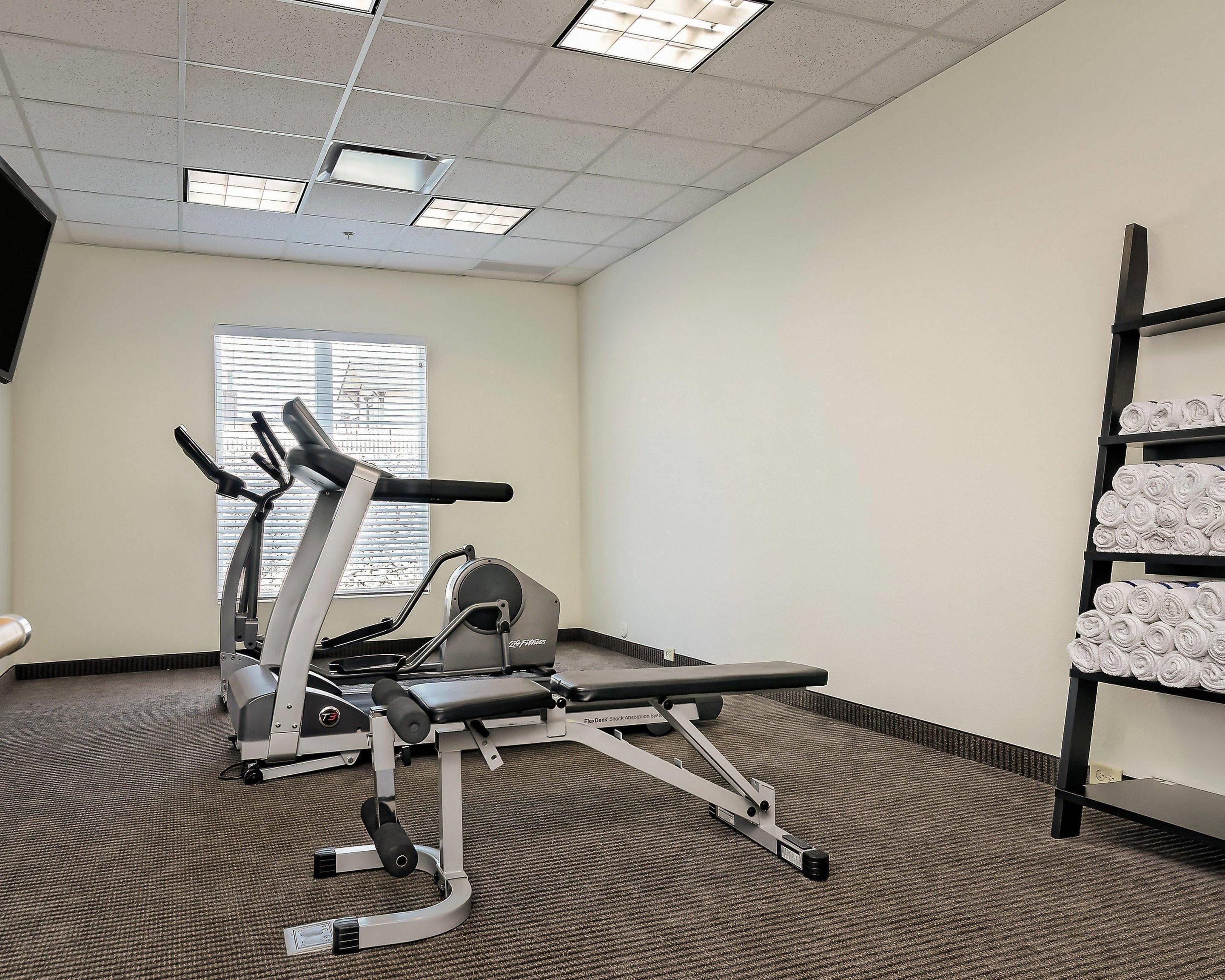 A gym with cardio equipment, a bench, and a rack of towels.