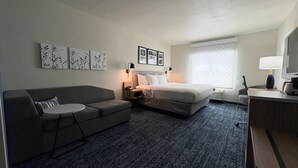 A hotel room with a bed, a sofa, a desk, a lamp, and wall art. - Sleep Inn & Suites Fort Scott (Fort Scott)