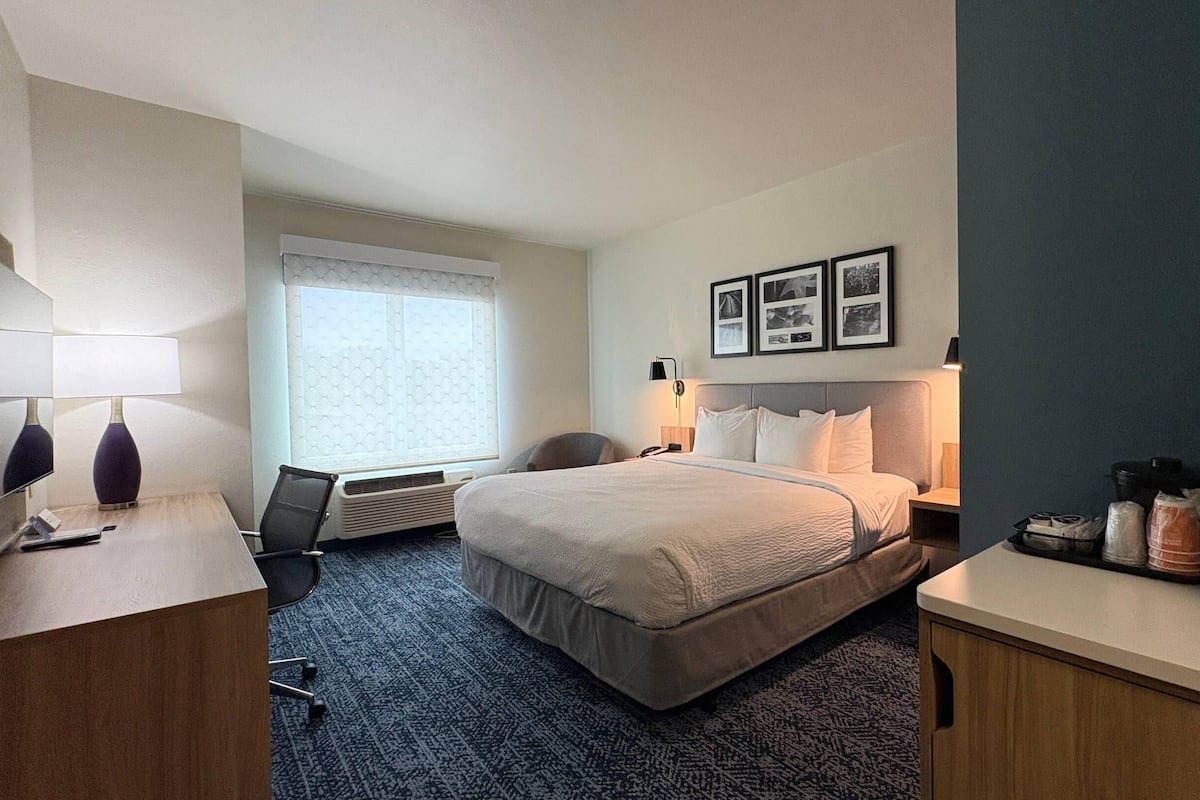 A hotel room with a bed, desk, chair, and a coffee machine.