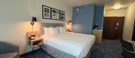 A hotel room with a bed, bedside tables, a desk, a chair, a wall-mounted phone, and framed pictures.