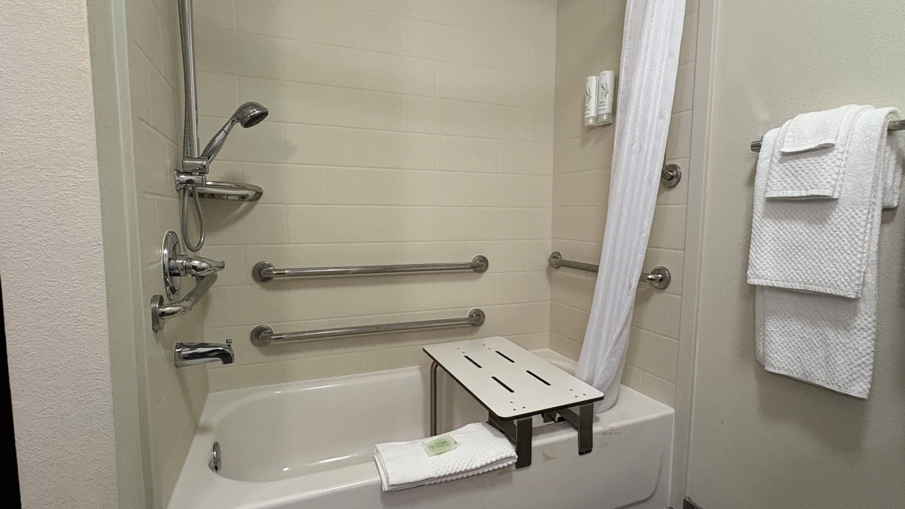 A bathroom with a bathtub, grab bars, a towel rack, and a showerhead.