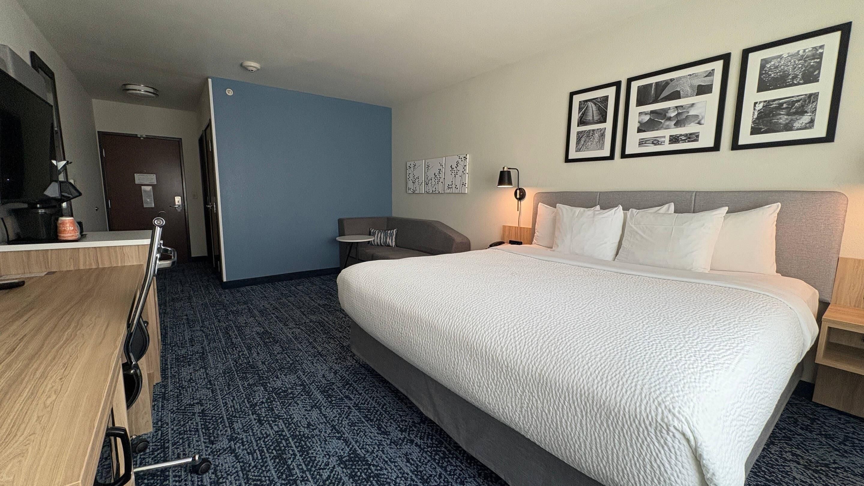 Ein Hotelzimmer mit einem großen Bett, einem Schreibtisch, einem Stuhl, einer Couch und einem Fernseher.