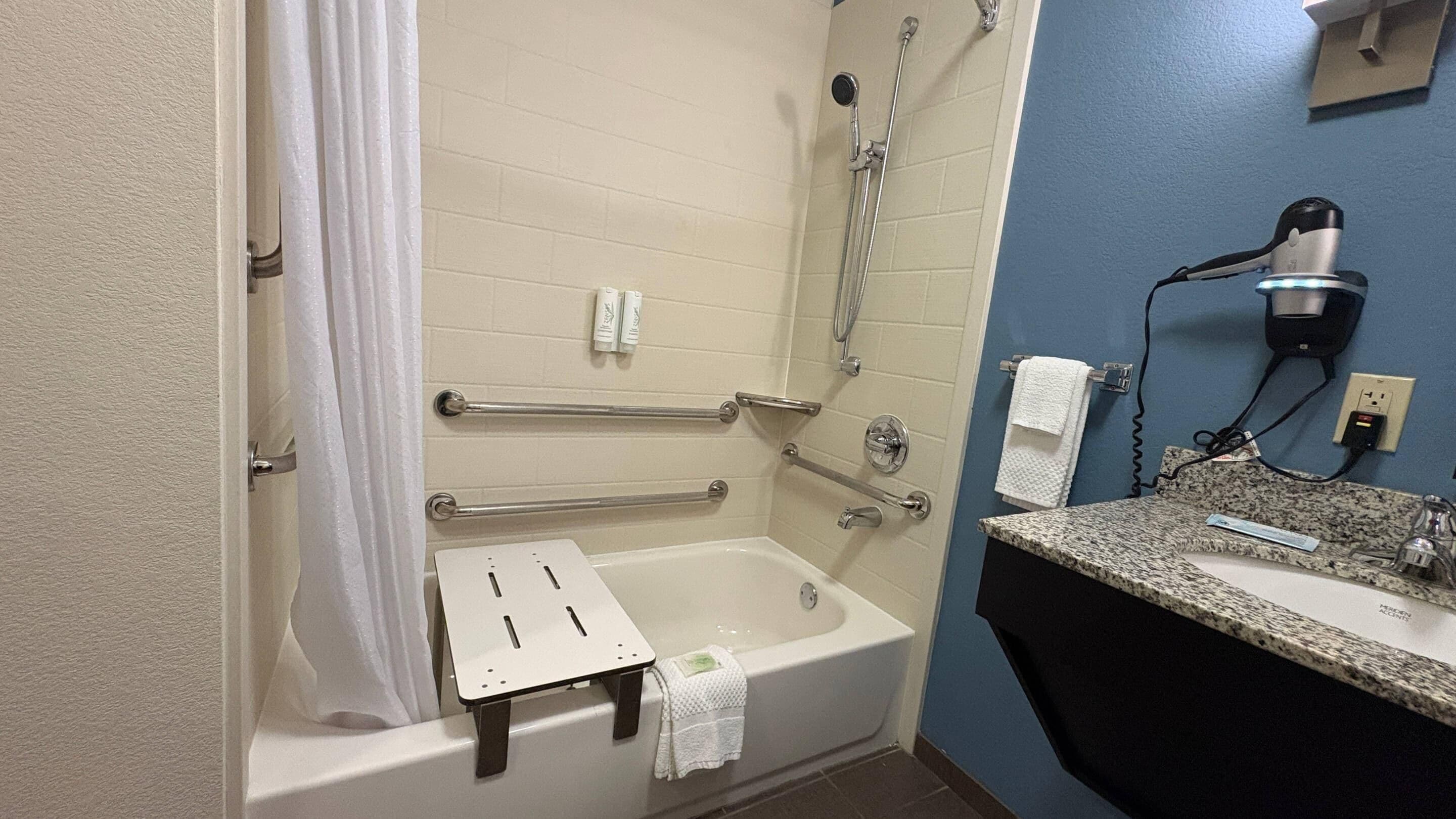A bathroom with a bathtub, grab bars, a shower, a sink, and a towel rack.