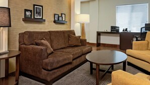 A modern living room with a brown sofa, a round coffee table, a yellow armchair, a desk with a computer, and wall-mounted picture frames. - Sleep Inn & Suites Fort Scott (Fort Scott)