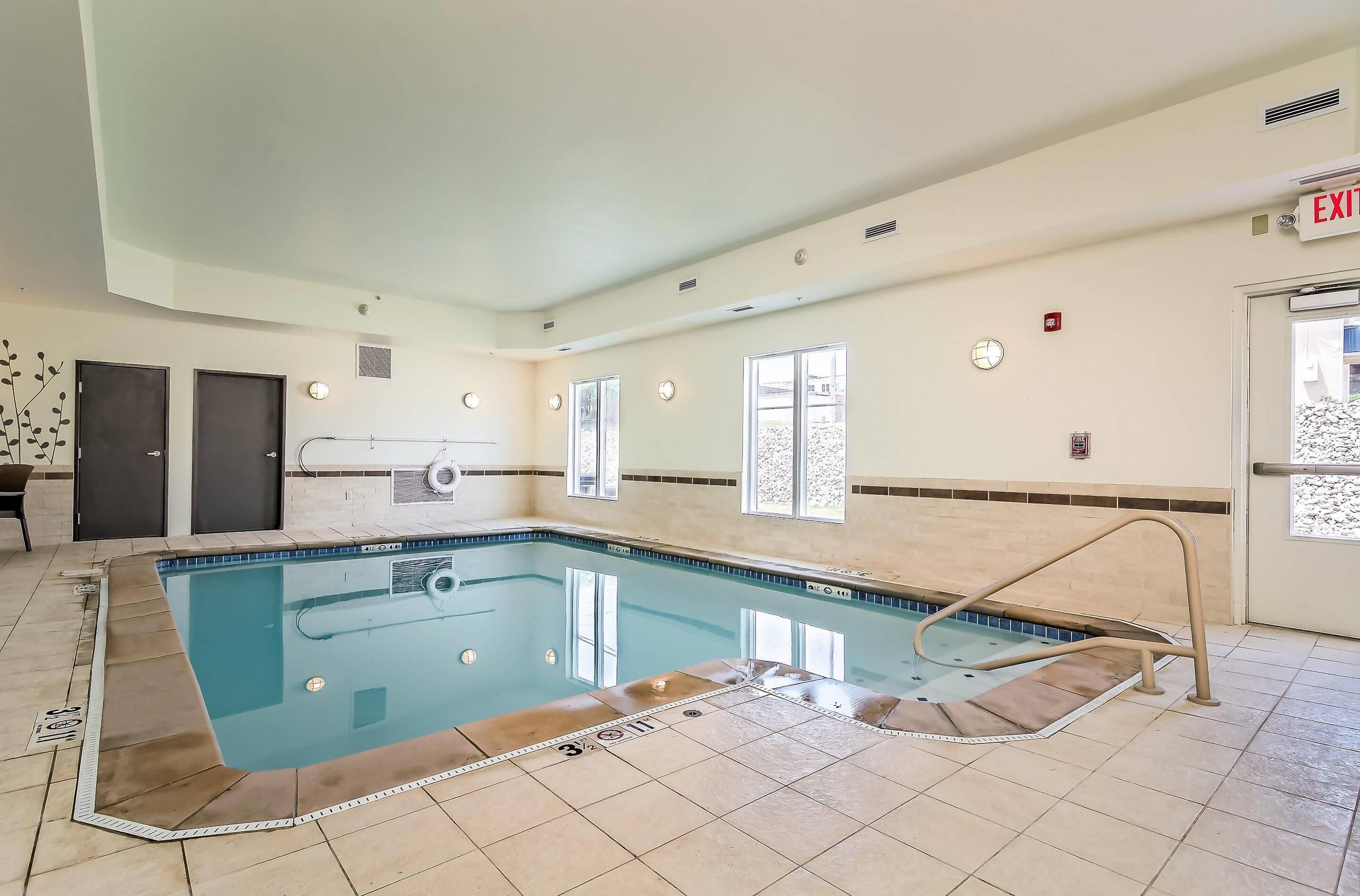An indoor swimming pool with a tiled floor, a pool ladder, and an exit sign.