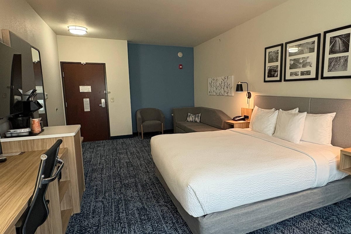 A hotel room with a bed, bedside tables, a desk, a chair, a coffee maker, and framed pictures on the wall.