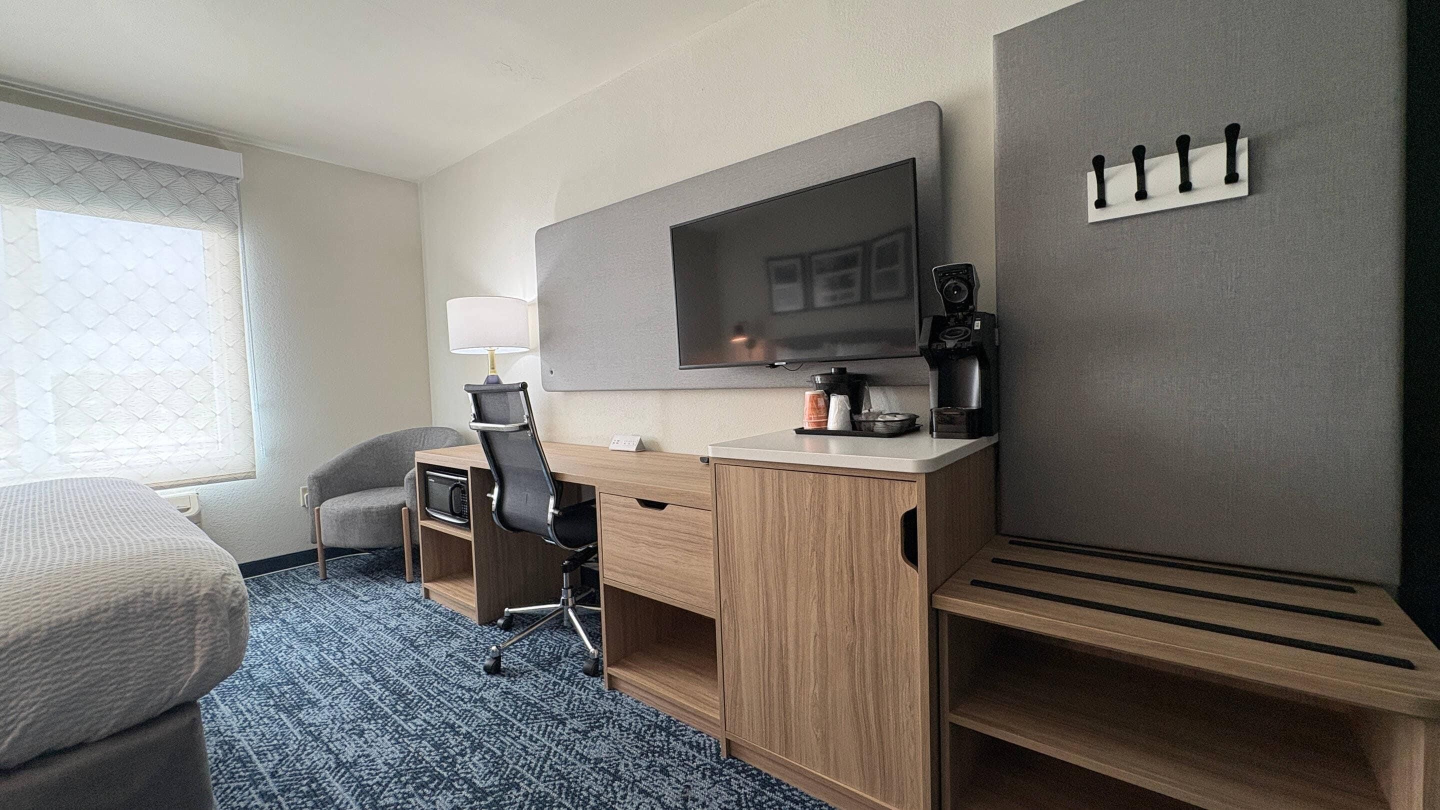 Habitación de hotel con cama, escritorio con silla, televisor, cafetera y máquina de café empotrada.