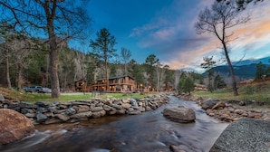 A lodge with a stone retaining wall and a stream in front. - 4 Seasons Inn on Fall River (Estes Park)