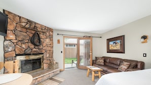 A cozy living room with a stone fireplace, a comfortable couch, a small wooden table, and a large bed. - 4 Seasons Inn on Fall River (Estes Park)