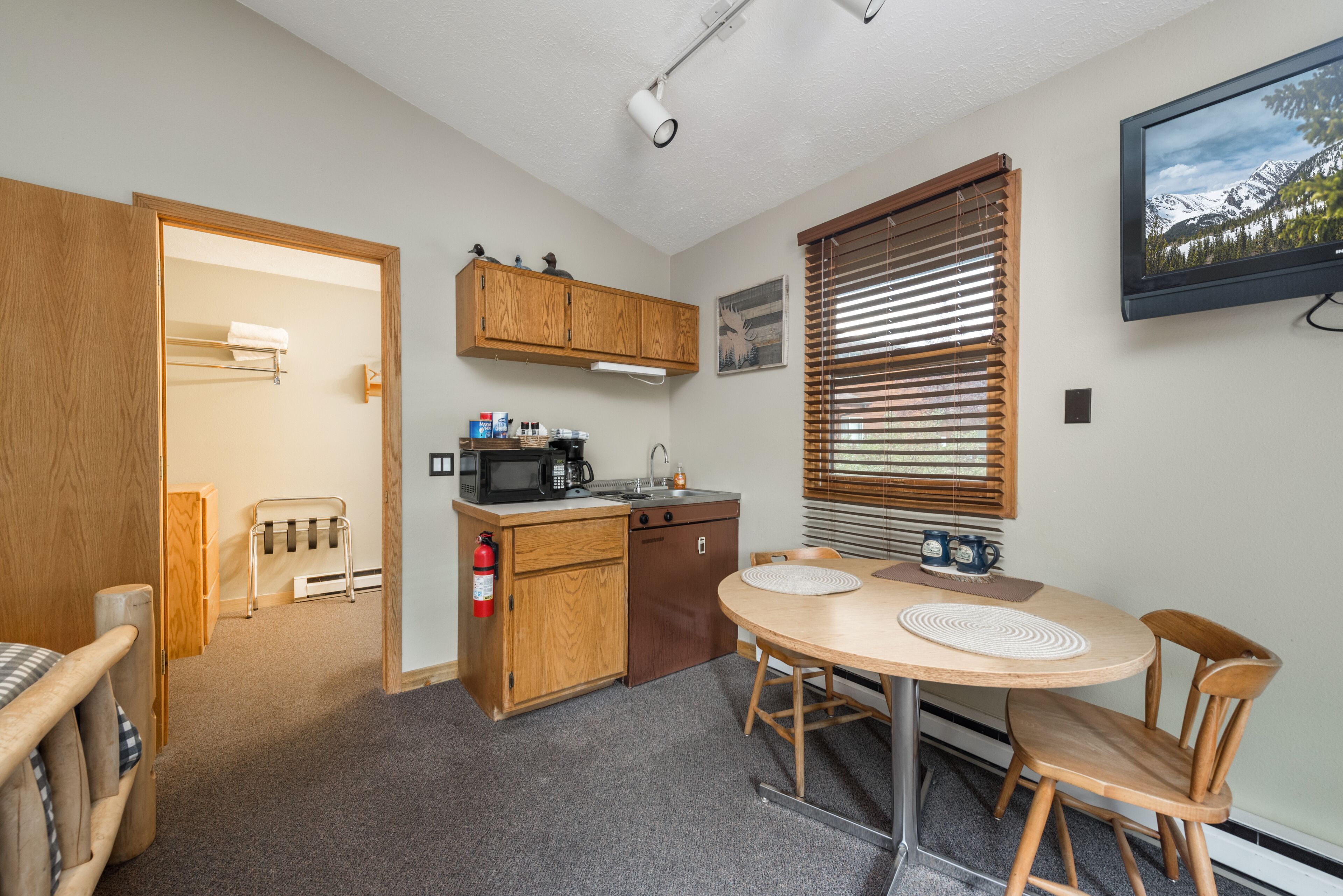 A compact kitchen with wooden cabinets, a microwave, a sink, and a small dining table with chairs.