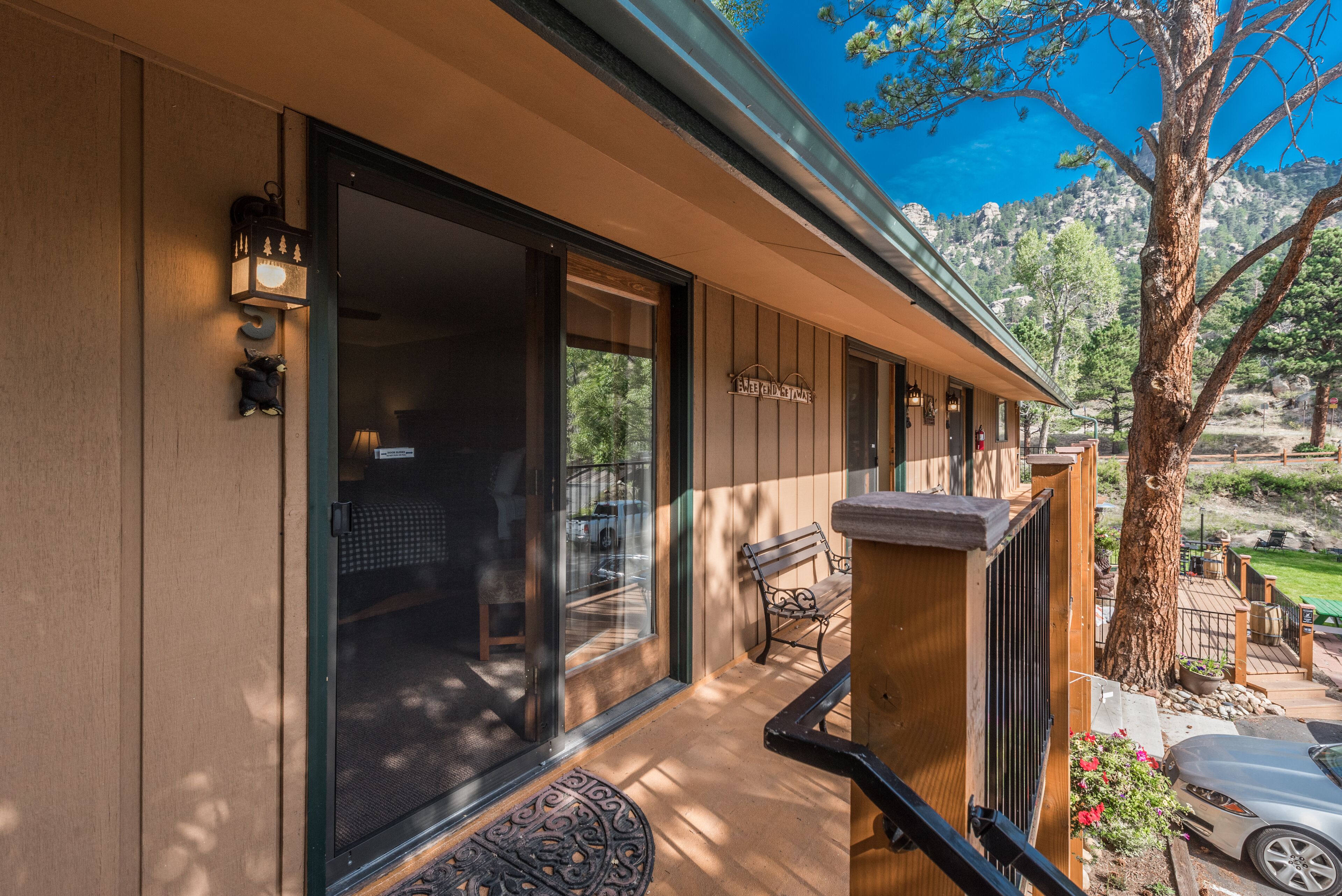 A wooden exterior with a glass door, a bench, and a tree.