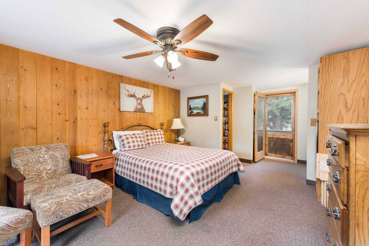A bedroom with a bed, a chair, a nightstand, a ceiling fan, and a wooden wardrobe.
