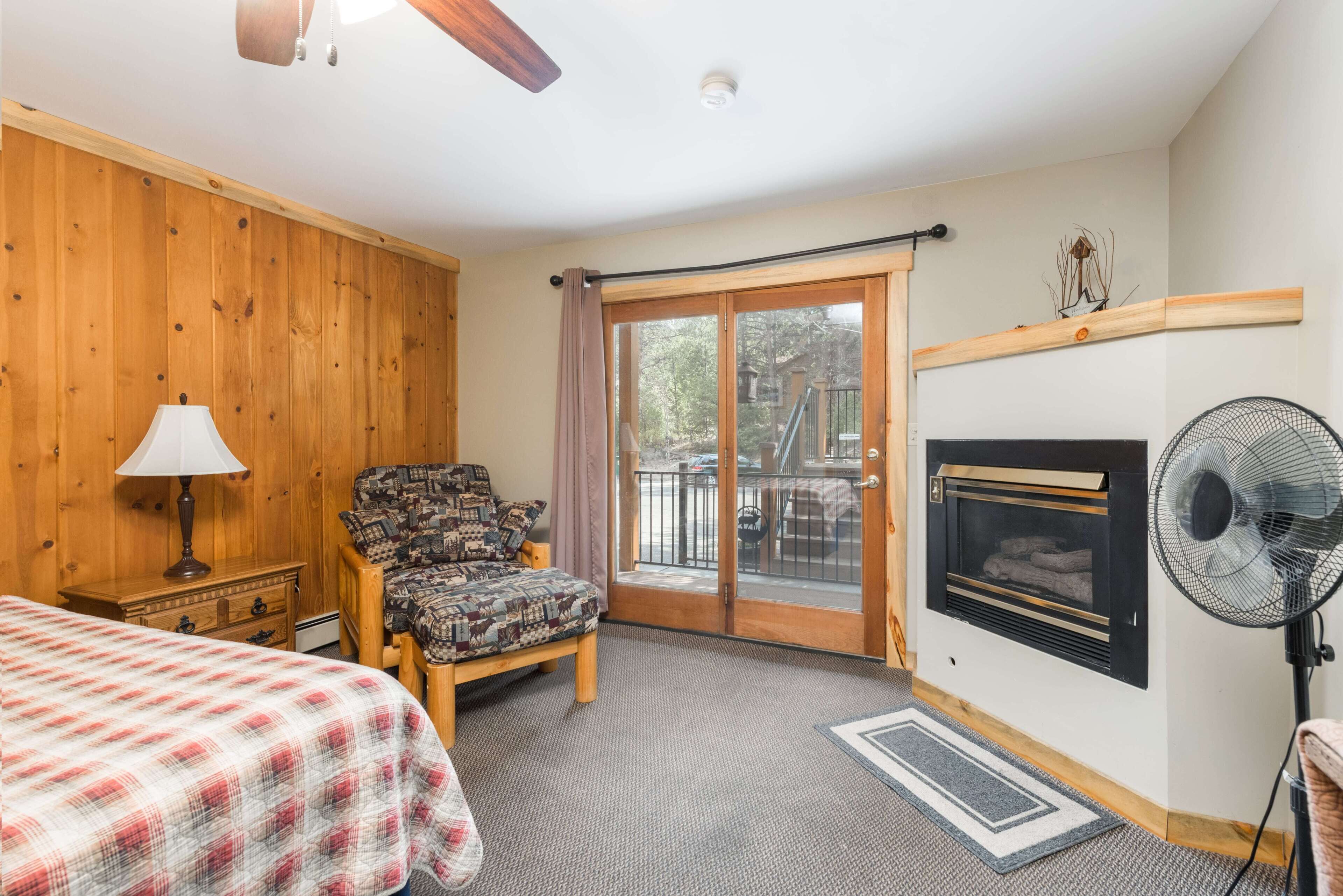 Una habitación con cama, sillón, chimenea y ventilador.
