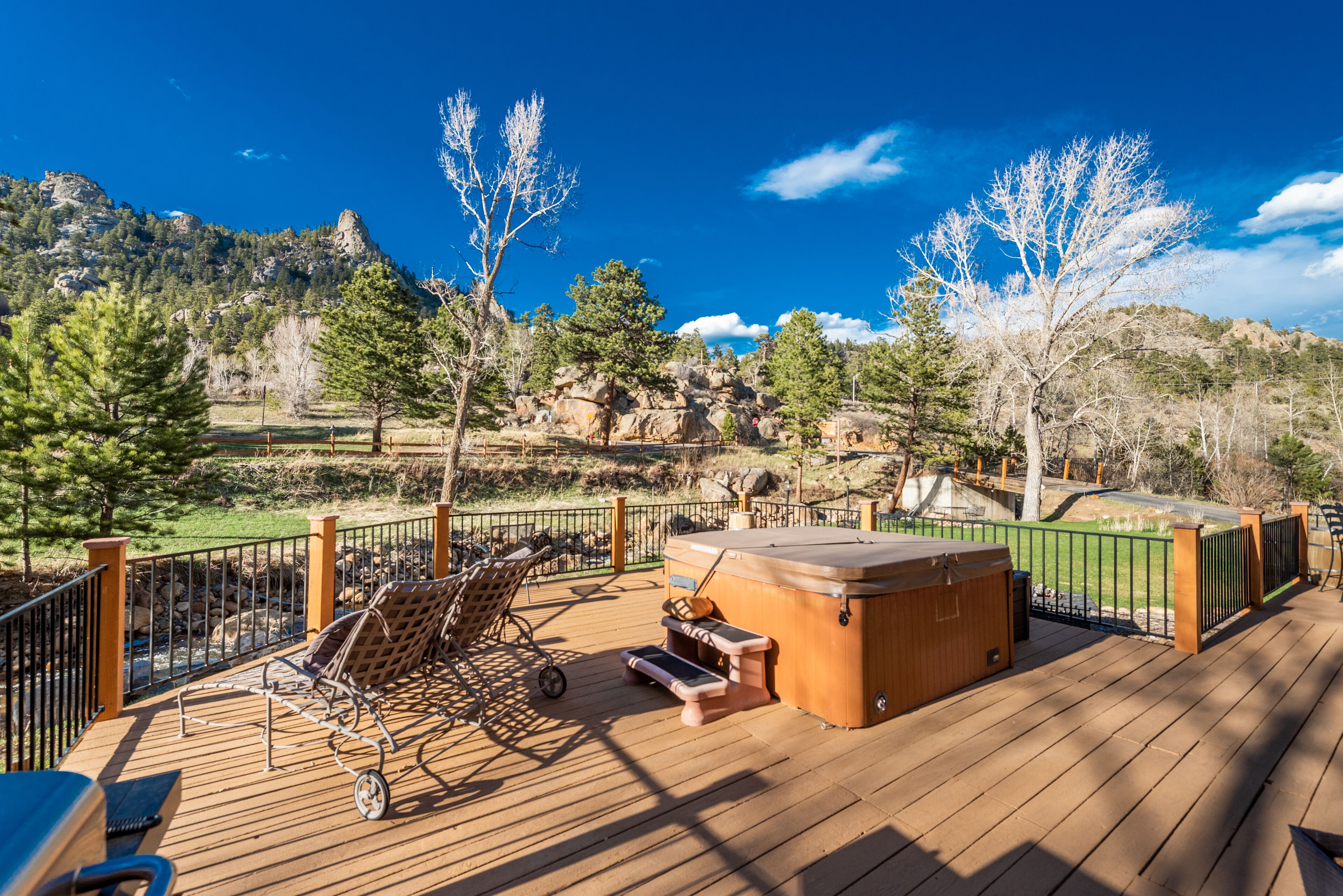 Una terraza de madera con mobiliario exterior, un jacuzzi y vistas a un paisaje montañoso.