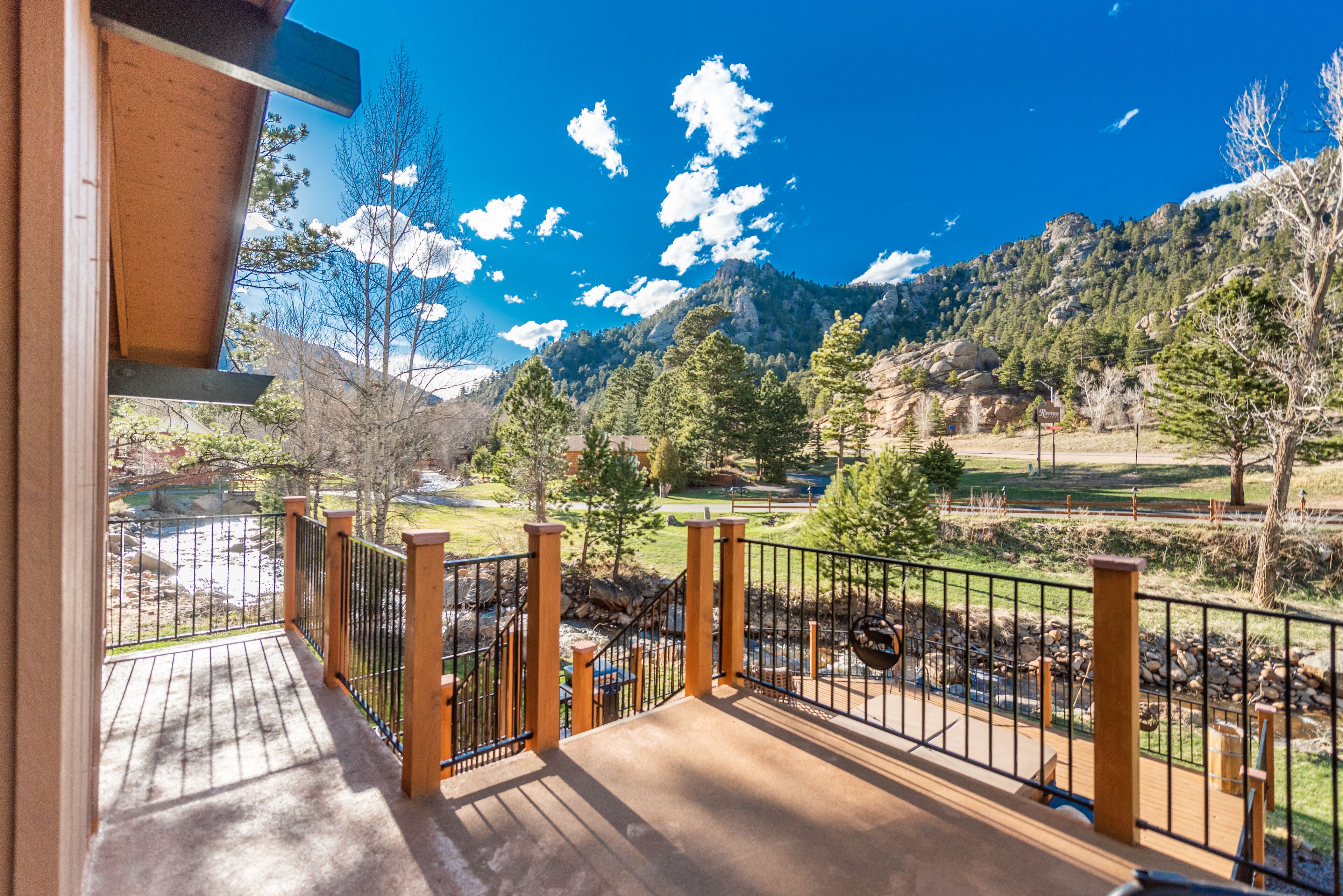 Un balcon doté d’une balustrade en bois, offrant une vue sur un paysage montagneux, avec des arbres et un ciel dégagé.