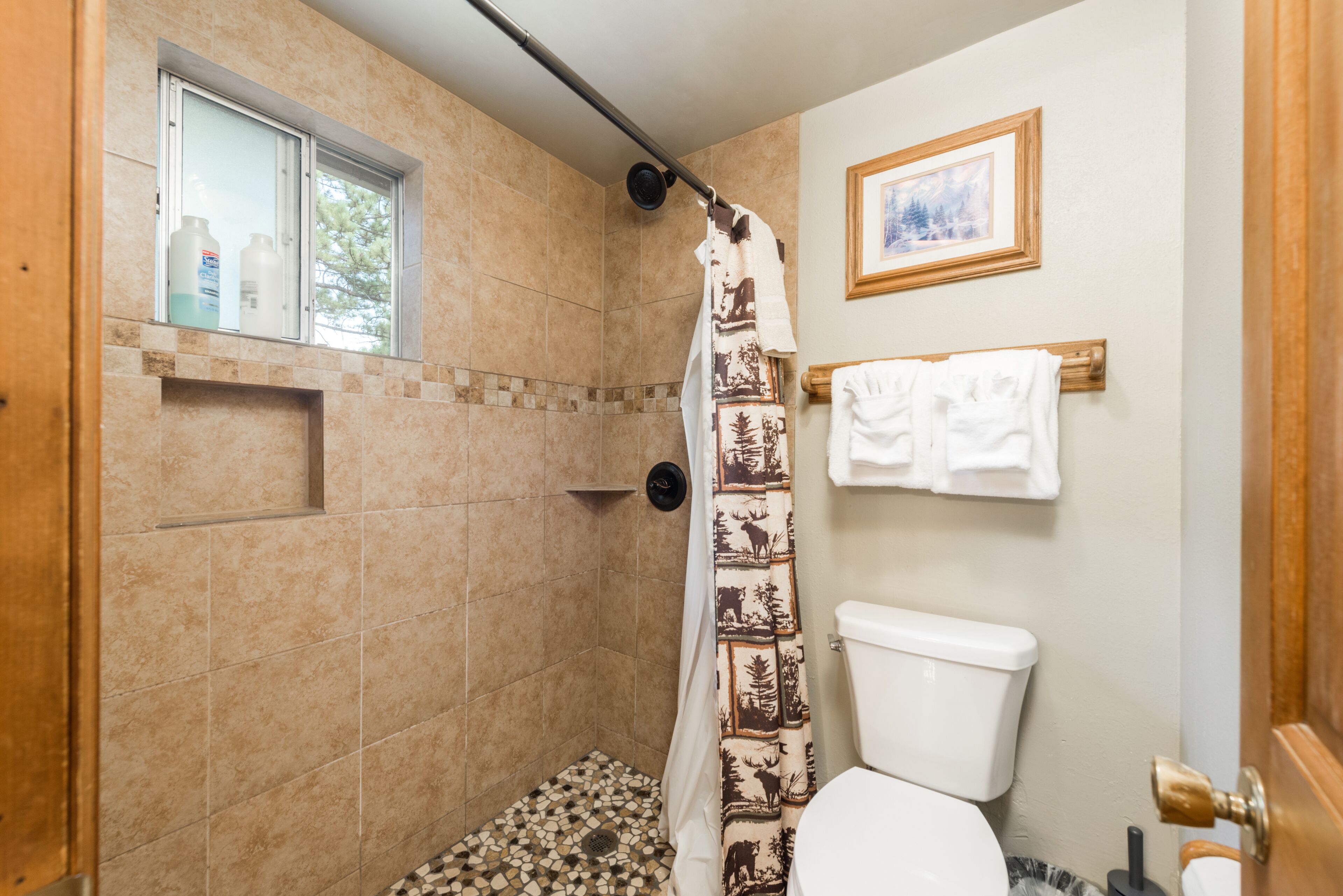 Une salle de bain avec une douche, des toilettes et une fenêtre sur laquelle sont posées des bouteilles.