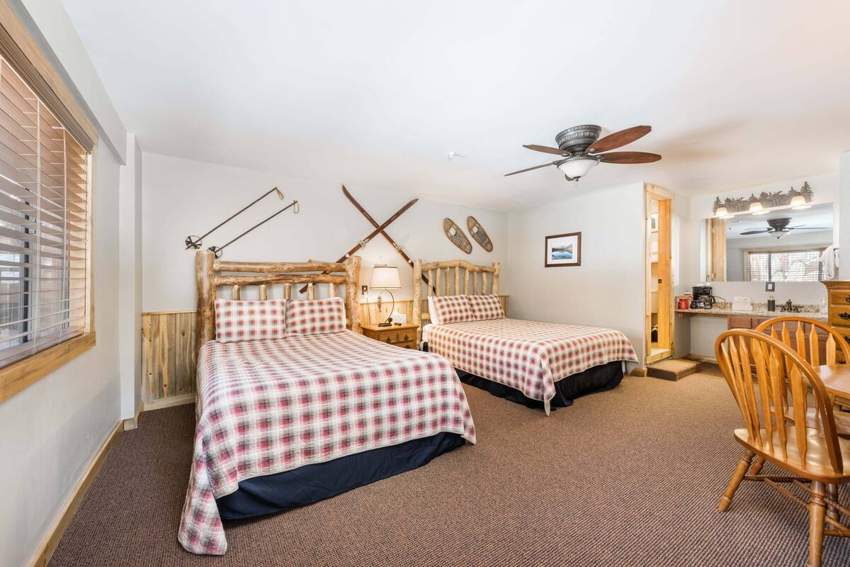 A room with two beds, a ceiling fan, a wooden chair, and a small table.