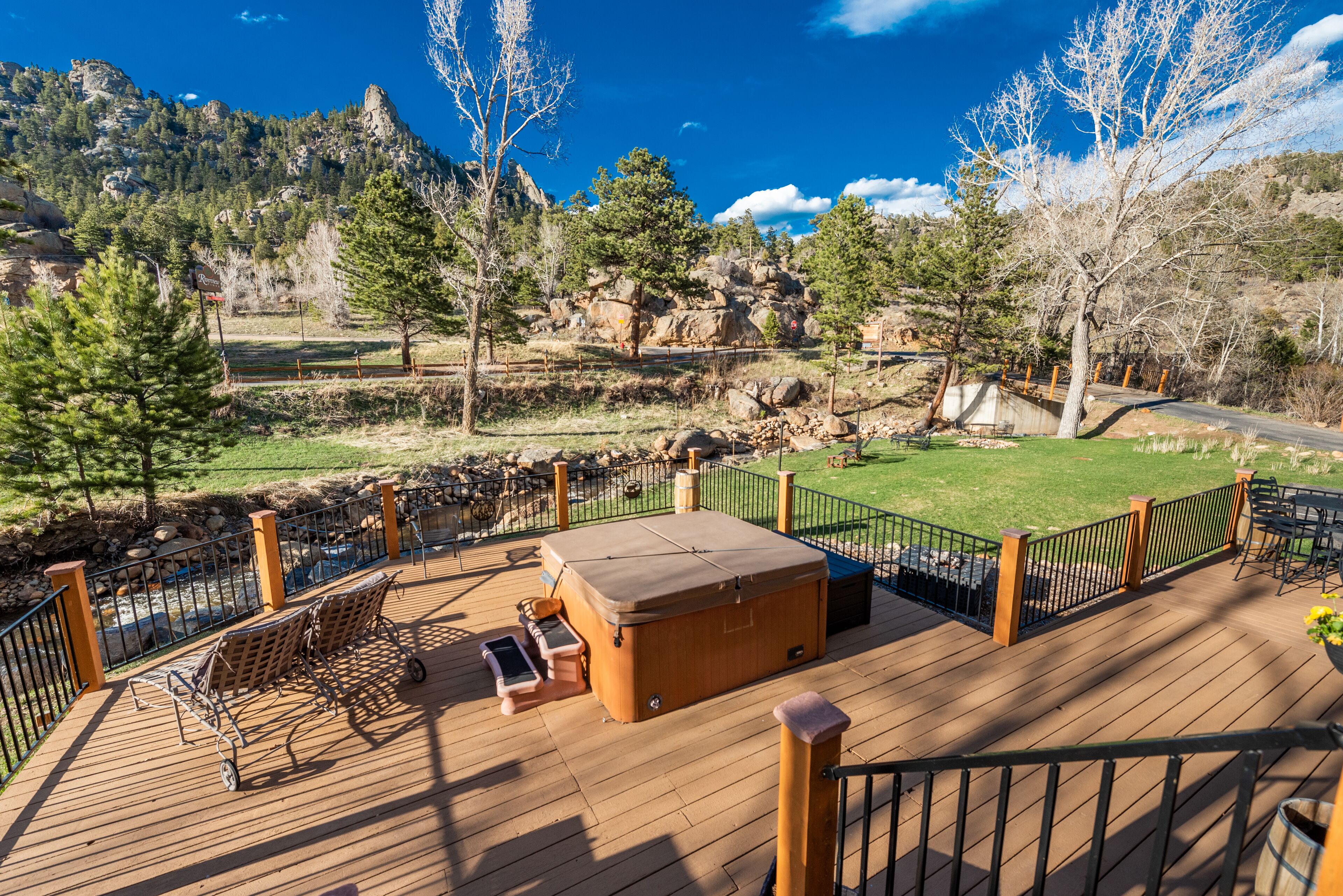 A wooden deck with a hot tub, lounge chairs, and a view of a mountainous landscape.