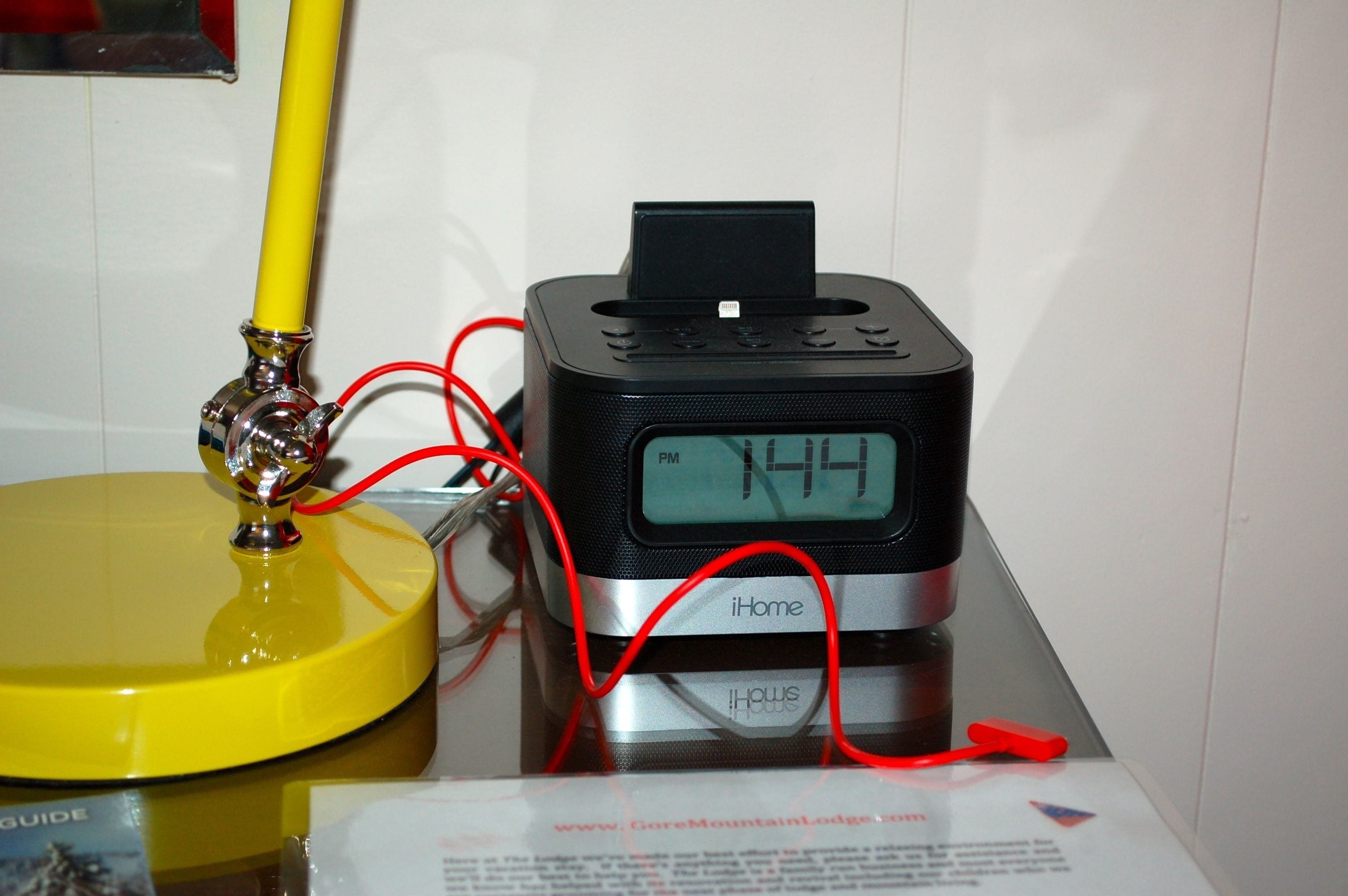 En digital klocka som visar 14:44, ansluten till en gul lampa med röda kablar, och en svart apparat med en kontakt på ovansidan.