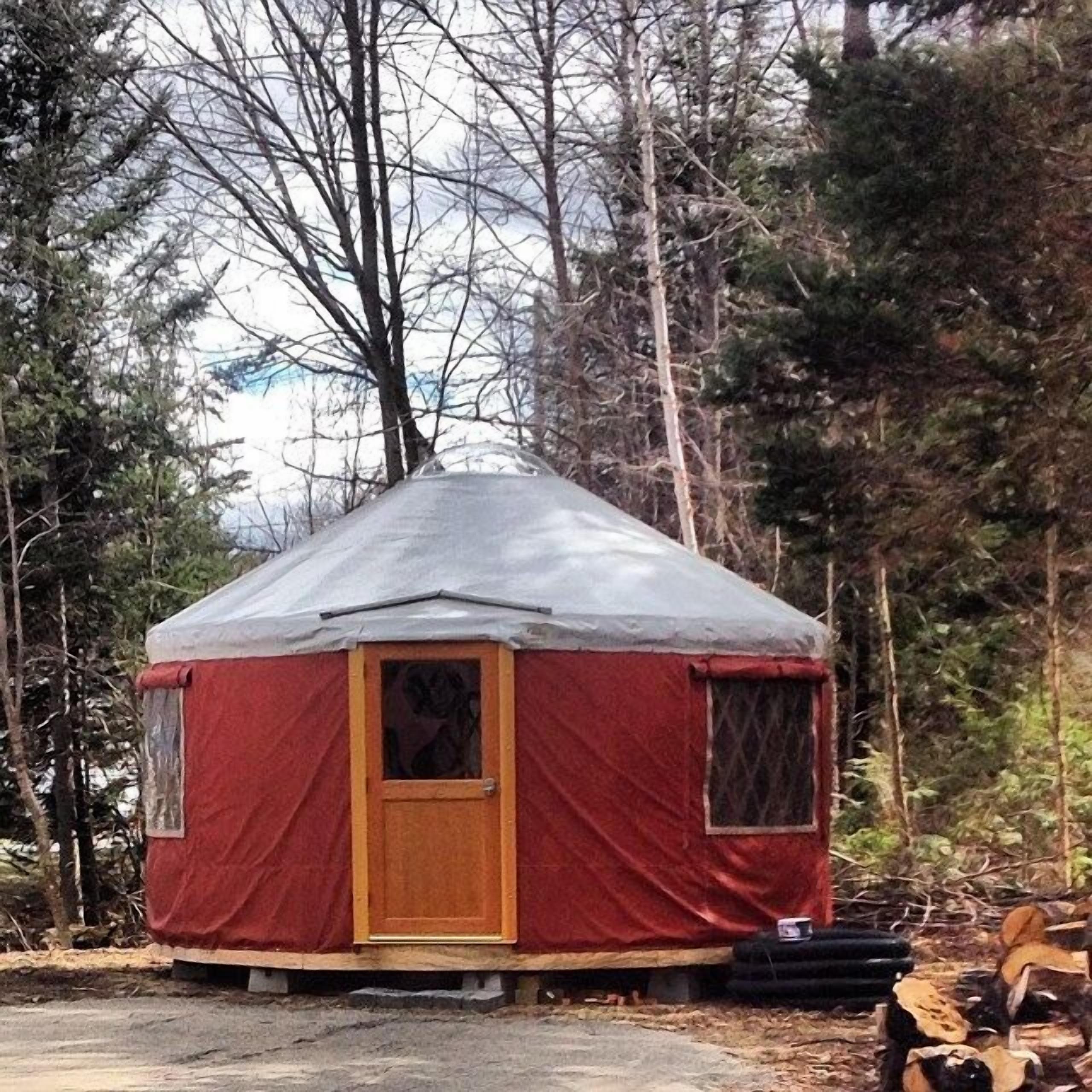 Uma yurt vermelha com porta e janelas de madeira, rodeada por árvores.