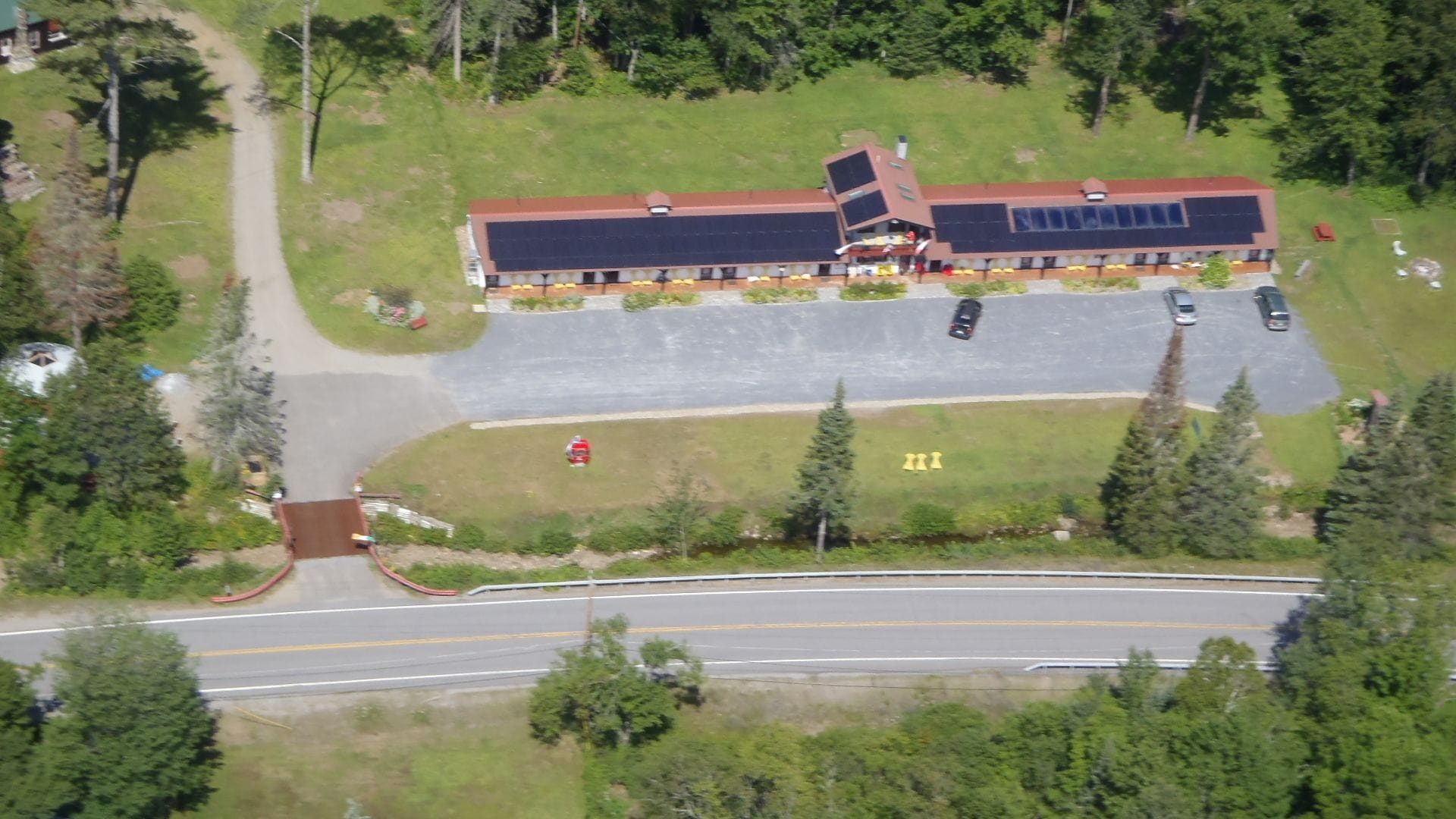 An aerial view of a building with a parking lot, a road in front, and surrounding greenery.