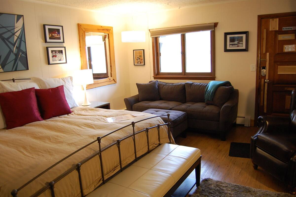 A bedroom with a bed, a sofa, a chair, and a window.