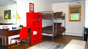 Un dormitorio con literas, un escritorio con silla, un estante rojo, un espejo y una ventana.