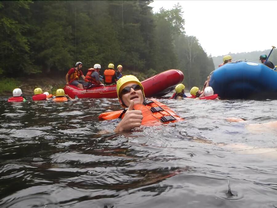 A group of people on inflatable rafts in a river surrounded by trees.