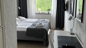 Una habitación de hotel con cama, mesita de noche, escritorio y ventana con cortinas.