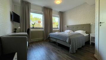 Habitación de hotel con cama, escritorio, silla, televisor y ventana con cortinas.
